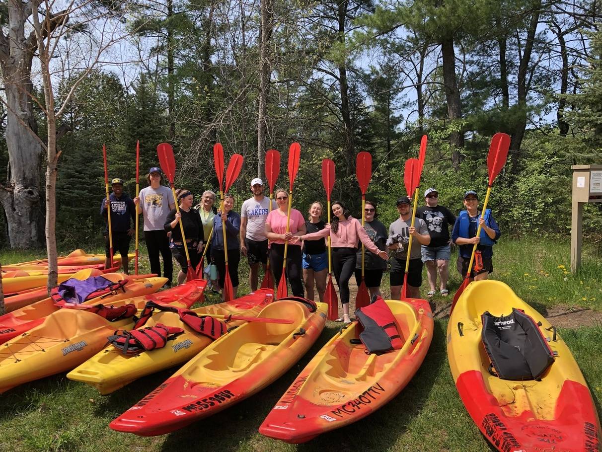 A row of people standing in front of a row of kayaks with oars in their hands